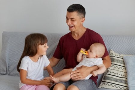 indoor-shot-happy-family-smiling-father-playing-with-two-daughters-sofa-cute-baby-biting-toy-d...jpg