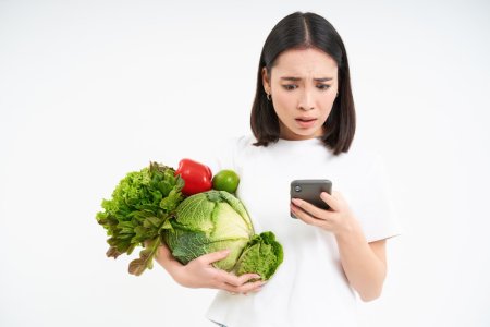 portrait-asian-woman-looks-worries-smartphone-screen-holds-vegetables-orders-food-online-white.jpg