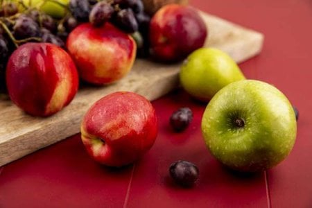 compressed-side-view-fresh-fruits-such-as-peachgrapeapple-wooden-kitchen-board-red-background.jpeg