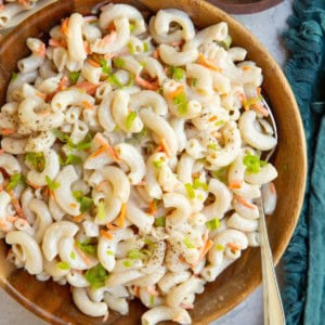 Wooden bowl full of macaroni salad with small bowls of salad and a bowl of chopped green onions