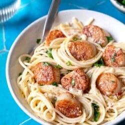 Bowl of pasta with scallops, lemon zest, and parsley on a blue tile background.