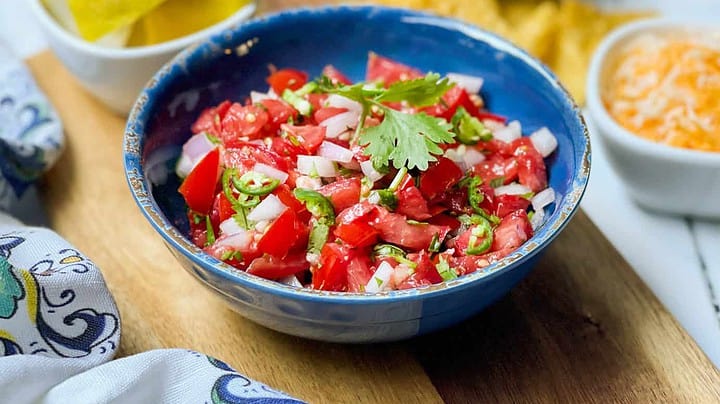 Side view of Fresh Salsa recipe in a blue bowl with chips and cilantro