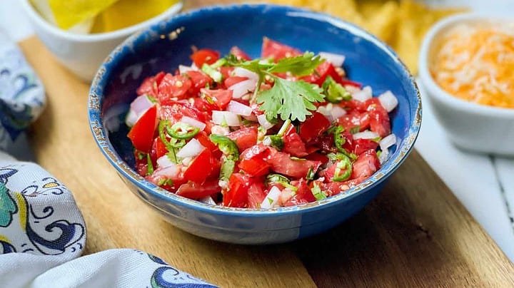 Side view of Fresh Salsa recipe in a blue bowl with chips and cilantro