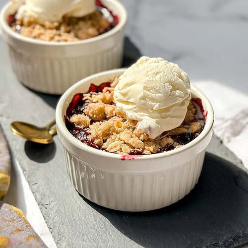 Side view of Individual Berry Crisps in a white ramekin on a black slate board.