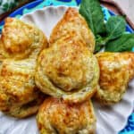 several baked Thai curry puff appetizers on a plate with side of Thai basil.