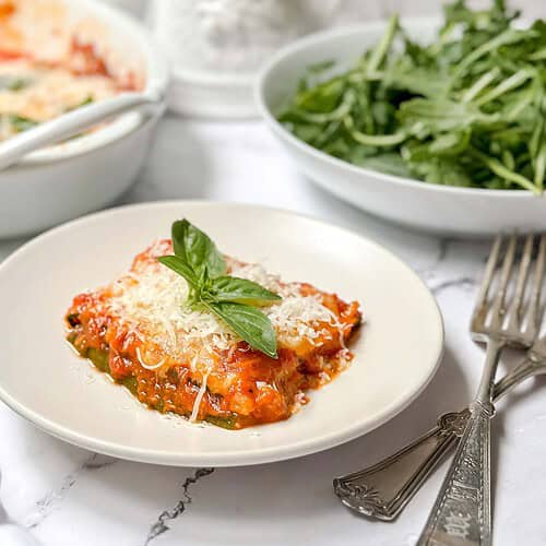 Horizontal side view of zucchini parmesan serving on a white plate with fresh basil.