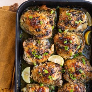 Finished garlic butter chicken thighs in a large roasting pan with chopped green onions and half a lemon to the side.