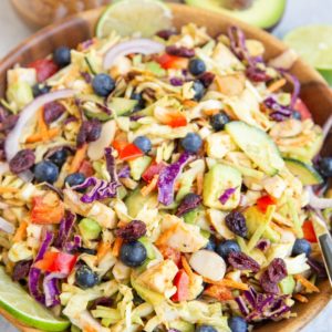Big salad bowl with cabbage salad inside. Jar of peanut dressing and avocado in the background. Big salad bowl with cabbage salad inside. Jar of peanut dressing and avocado in the background.